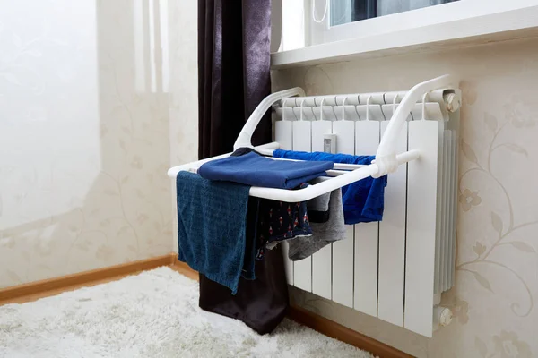 Clothes dryer. Blue clothes is fixed to dry after washing at home on battery. Idea for saving space, home routine, lifestyle concept. Useful hanging interior device. Hot radiator. Secondary used heat.