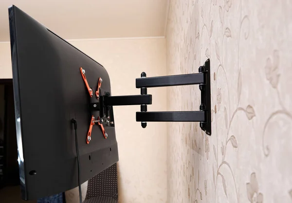 Dön TV ayraç LED ekran. Arkadan bak. X şeklinde kırmızı bağlayıcılar. Siyah renk. Çok düzlemli. Duvarda asılı. Güvenilir ve rahat bağlanma. Çocuk korumalı ve yuvarlanma korumalı. Metalik ekipman.