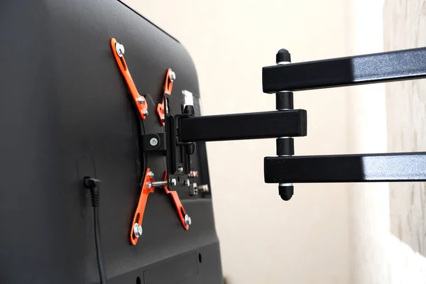 Dön TV ayraç LED ekran. Arkadan bak. X şeklinde kırmızı bağlayıcılar. Siyah renk. Çok düzlemli. Duvarda asılı. Güvenilir ve rahat bağlanma. Çocuk korumalı ve yuvarlanma korumalı. Metalik ekipman.