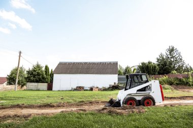Bir patinaj dümeni yükleyicisi inşaat için alanı boşaltıyor. Arazi işleri arazi iyileştirmesi ile yapılır. Kapalı alanlarda çalışmak için bir makine. Toprak, çim ve malzeme taşımak için kovası olan küçük bir traktör..