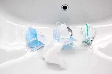 Kullanılmış tıbbi maskeler lavaboda yıkanmayı bekliyor. Beyaz renkli banyo. Tekrar kullanılmak üzere para biriktirip dezenfekte etmek. Tekrar kullanılabilir. Aile sağlık hizmetleri ve bütçe kavramını koru. Salgın hijyen..