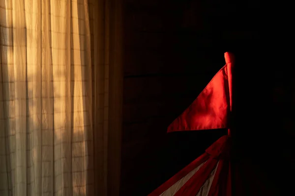 Red flag from a children\'s play tent in the rays of sunlight on dark background. Baby game room toy. Calm morning time. Sunrise. Win concept. Triangular shape. Evening sunset. First rays. Copy space.