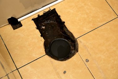 Lağım temizliği. Tesisatçı tıkanıklığı temizlemek için lağım yılanı kullanır. Tuvalet tamiri. Kanalizasyon borusu. Yerde bir delik. Kötü kokuyor. Kirli su. Sarı kiremitler. Tesisat hatası. ÇEVİR.