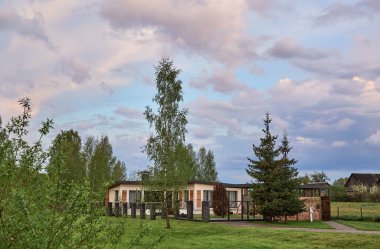 Ön cephesinde tahta kaplama elementleri olan tek katlı bir bina. Komşuları olmayan köy evi. Metal profillerden yapılmış düz bir çatı. Gabion taşı ve siyah galvanize ağdan yapılmış birleşik çit..