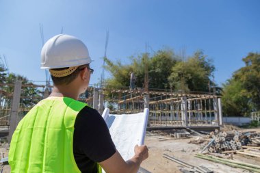 Mühendisler kask takıyor ve inşaat planını tutuyor..