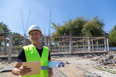 Mühendisler miğfer takıyor ve inşaat planını ve tableti tutuyor..