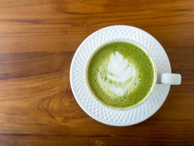 Ahşap masada fotokopi alanı olan sıcak yeşil çay. Barista fincanın üzerine köpükle latte yaprağı şekli çizer. Üst görünüm.