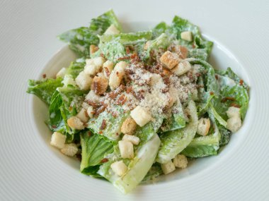 Restoranda, beyaz tabakta, tahta masada Sezar salatası..