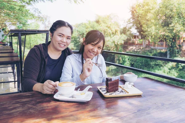 Mother and daughter eat chocolate cake and coffee and tea in restaurant.