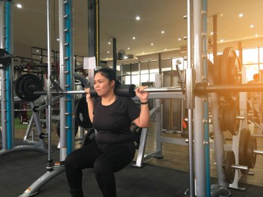 Asyalı şişman kız spor salonunda halter teçhizatıyla ağırlık ve kilo vermek için eğitiliyordu..