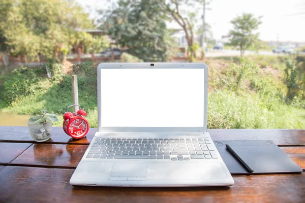Computer laptop and mouse pen on wood table outdoor and nature background. The blank screen with copy space for your text or advertising content. Selective focus and clipping path on picture.
