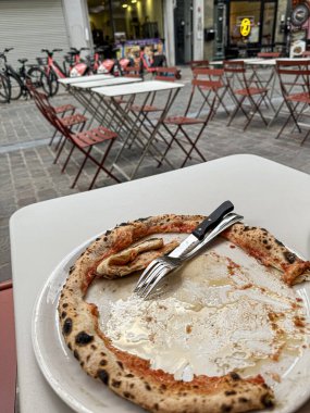 Açık hava restoranındaki yemek artıkları, çatal ve bıçakla dolu boş bir pizza tabağı, yemeğin bittiğini gösteriyor.
