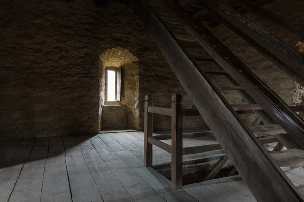 Habitación oscura con paredes de piedra ventana y escalera de madera — Foto de Stock