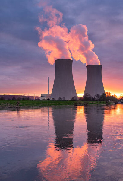 Атомная электростанция против неба у реки на закате