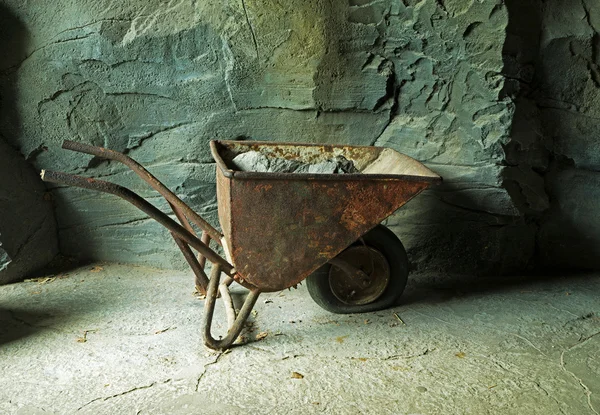 Παλιό σκουριασμένο wheelbarrow με μεταλλεύματος στο ορυχείο στο πέτρινο τοίχο — Φωτογραφία Αρχείου