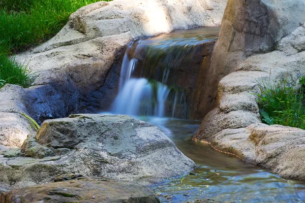 Waterfall on the creek flowing through  green grass — Stock Photo, Image