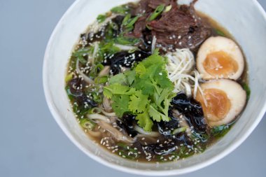 Bir kase Asya erişteli ramen çorbası, taze soğan, dilimlenmiş yumurta ve siyah masada mantar. Japon yemeği siyah.