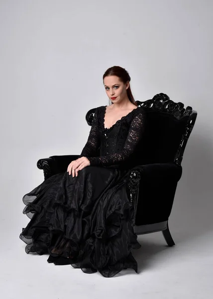Pełnowymiarowy Portret Kobiety Czarnej Gotyckiej Sukience Siedzącej Ozdobnym Czarnym Fotelu — Zdjęcie stockowe