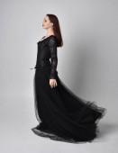 Ganzkörperporträt einer Frau in schwarzem Gothikkleid, im Stehen vor Studiohintergrund.