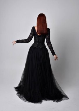 Siyahi gotik elbise giyen, arka planda kameraya poz veren bir kadının tam boy portresi..