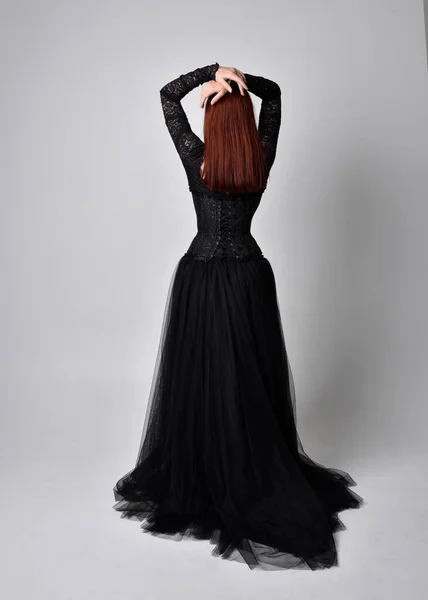 黒いゴシックのドレスを着た女性の完全な長さの肖像画 スタジオの背景にカメラに背を向けて立ちポーズ — ストック写真