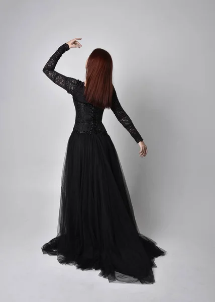 身穿黑色哥特式连衣裙的女人的全长肖像 背对着摄像机站在摄影棚后面 — 图库照片