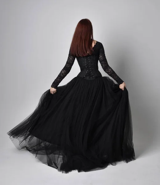 黒いゴシックのドレスを着た女性の完全な長さの肖像画 スタジオの背景にカメラに背を向けて立ちポーズ — ストック写真