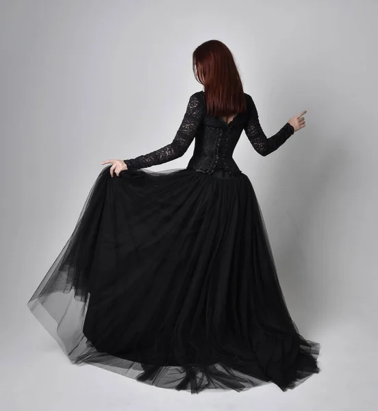 身穿黑色哥特式连衣裙的女人的全长肖像 背对着摄像机站在摄影棚后面 — 图库照片