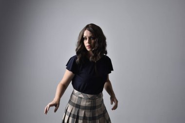 Close up portrait of pretty brunette woman wearing tartan skirt and blouse.  Posing with gestured hands against a  studio background. clipart