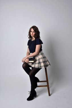 Tartan etek ve bluz giyen güzel esmer kadının yakın portresi. Stüdyonun arka planında poz vermek.