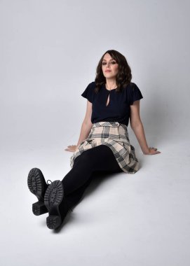 Uzun boylu, esmer, etek ve bluz giyen güzel bir kadının portresi. Stüdyonun arka planında, yerde oturuyor..