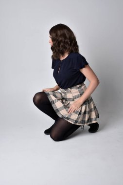 Uzun boylu, esmer, etek ve bluz giyen güzel bir kadının portresi. Stüdyonun arka planında, yerde oturuyor..