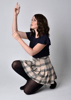 Uzun boylu, esmer, etek ve bluz giyen güzel bir kadının portresi. Stüdyonun arka planında, yerde oturuyor..