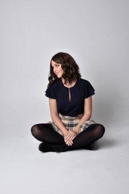 Uzun boylu, esmer, etek ve bluz giyen güzel bir kadının portresi. Stüdyonun arka planında, yerde oturuyor..