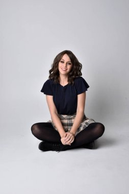 Uzun boylu, esmer, etek ve bluz giyen güzel bir kadının portresi. Stüdyonun arka planında, yerde oturuyor..