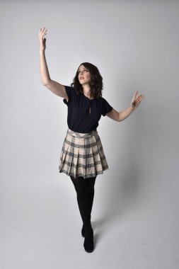 Uzun boylu, esmer, etek ve bluz giyen güzel bir kadının portresi. Stüdyonun arka planında, yerde duruyor..