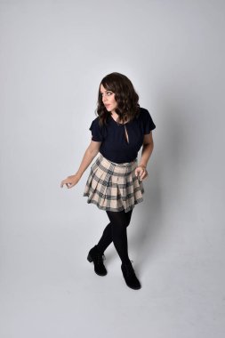 Uzun boylu, esmer, etek ve bluz giyen güzel bir kadının portresi. Stüdyonun arka planında, yerde duruyor..