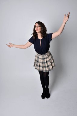 Uzun boylu, esmer, etek ve bluz giyen güzel bir kadının portresi. Stüdyonun arka planında, yerde duruyor..