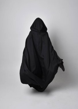 Uzun siyah saçlı, uzun siyah cüppeli güzel bir kadın portresi. Stüdyonun arka planında kameraya dönük poz vermek.