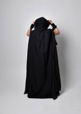 Uzun siyah saçlı, uzun siyah cüppeli güzel bir kadın portresi. Stüdyonun arka planında kameraya dönük poz vermek.