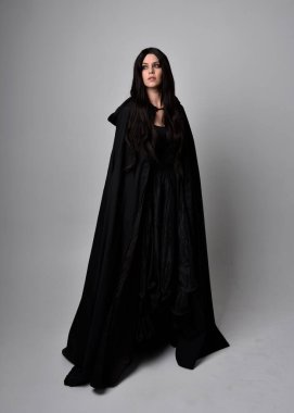 Uzun siyah saçlı, uzun siyah cüppeli güzel bir kadın portresi. Stüdyonun arka planında kameraya dönük poz vermek.