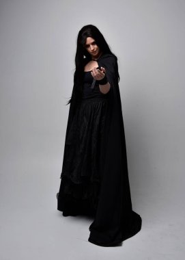 Uzun siyah saçlı, uzun siyah cüppeli güzel bir kadın portresi. Stüdyonun arka planında kameraya dönük poz vermek.