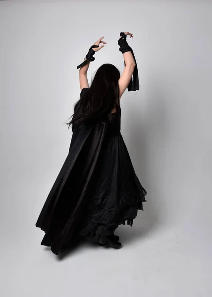 全长肖像漂亮的黑色头发女人穿着黑色长袍纳达斗篷 站在镜头前 面对着摄影棚的背景 — 图库照片