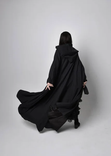 全长肖像漂亮的黑色头发女人穿着黑色长袍纳达斗篷 站在镜头前 面对着摄影棚的背景 — 图库照片