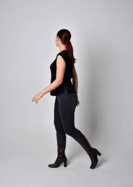 Sade, uzun, at kuyruklu, siyah tişört ve kot pantolon giyen kızıl saçlı bir kadın portresi. Kameraya dönük poz vermek, kamera, stüdyonun arka planında..
