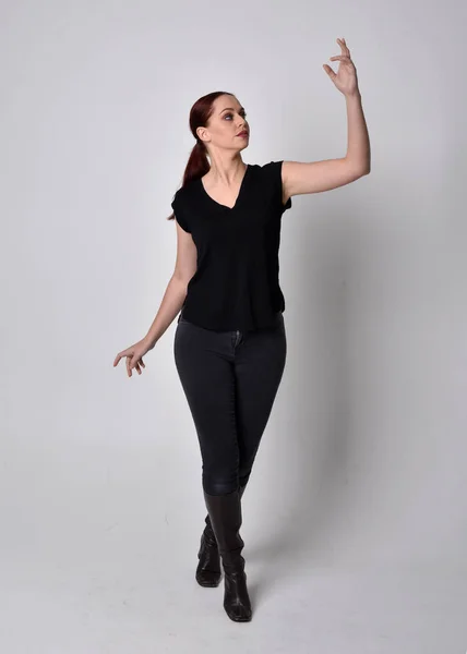 穿着宽松的黑色T恤和牛仔裤 头戴马尾辫 红头发的女人的简单全长肖像 在工作室的背景下 用手势站在前面 — 图库照片