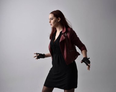 Kırmızı deri ceket ve eldiven giyen kızın yakın portresi. El hareketleriyle poz vermek, sanki büyü yapmak gibi. Moody arka planda bir stüdyoda ışıklandırma.