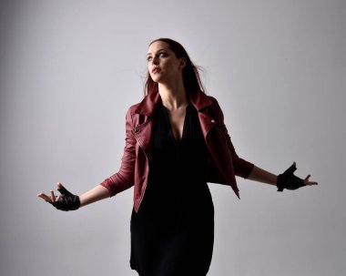 Kırmızı deri ceket ve eldiven giyen kızın yakın portresi. El hareketleriyle poz vermek, sanki büyü yapmak gibi. Moody arka planda bir stüdyoda ışıklandırma.