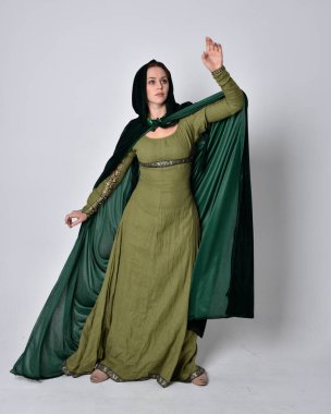 Fantezi kadife pelerinli yeşil ortaçağ elbisesi giyen kızıl saçlı kızın tam boy portresi. Stüdyonun arka planında yalnız poz vermek.