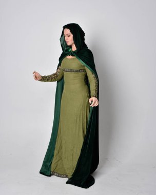 Fantezi kadife pelerinli yeşil ortaçağ elbisesi giyen kızıl saçlı kızın tam boy portresi. Stüdyonun arka planında yalnız poz vermek.